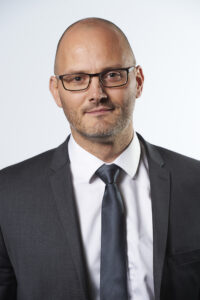 Headshot featuring Jakob Juul Rasmussen, co-founder and managing director of Pharma IT, wearing a dark grey suit, white dress shirt, and dark grey neck tie.